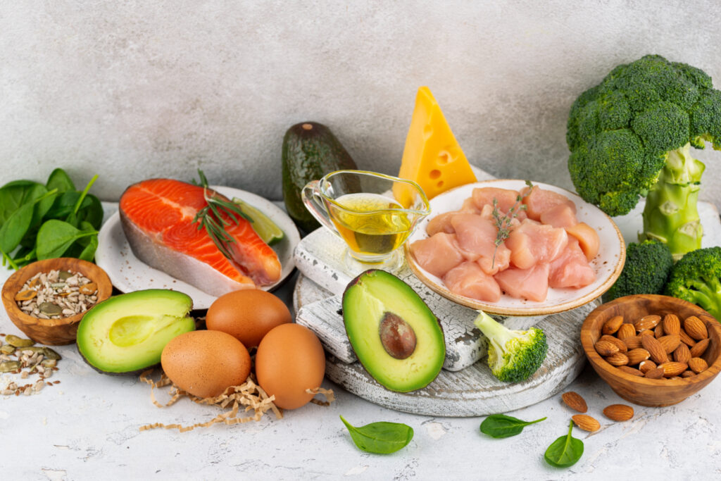 A variety of healthy fats including avocado, nuts, seeds, olive oil, and salmon on a wooden table.