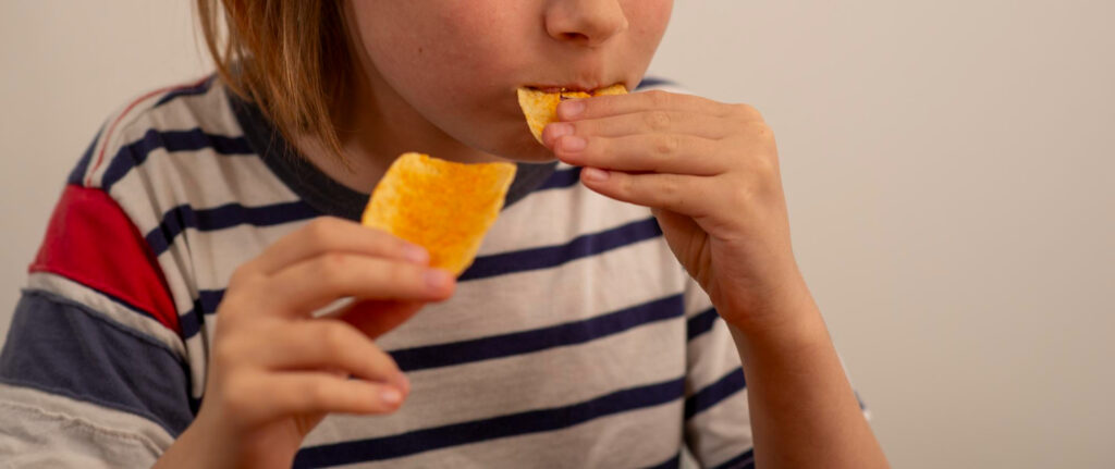 A 10-year-old boy happily eating a bag of chips.