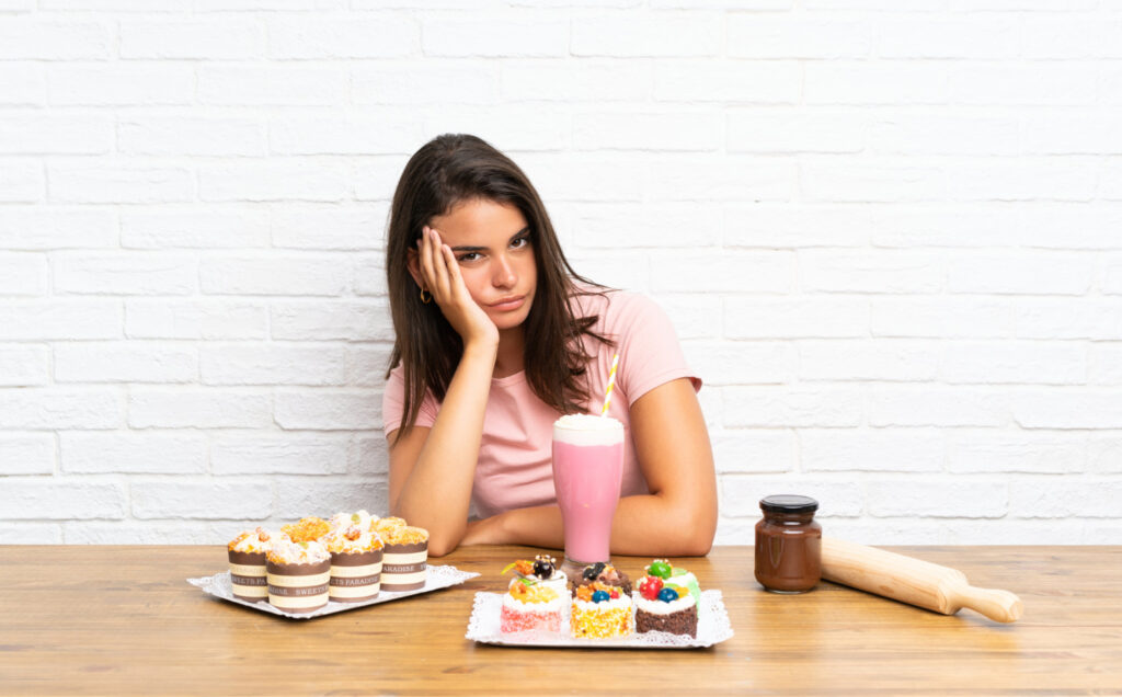 A young girl looking unhappy and frustrated in front of a variety of mini cakes.